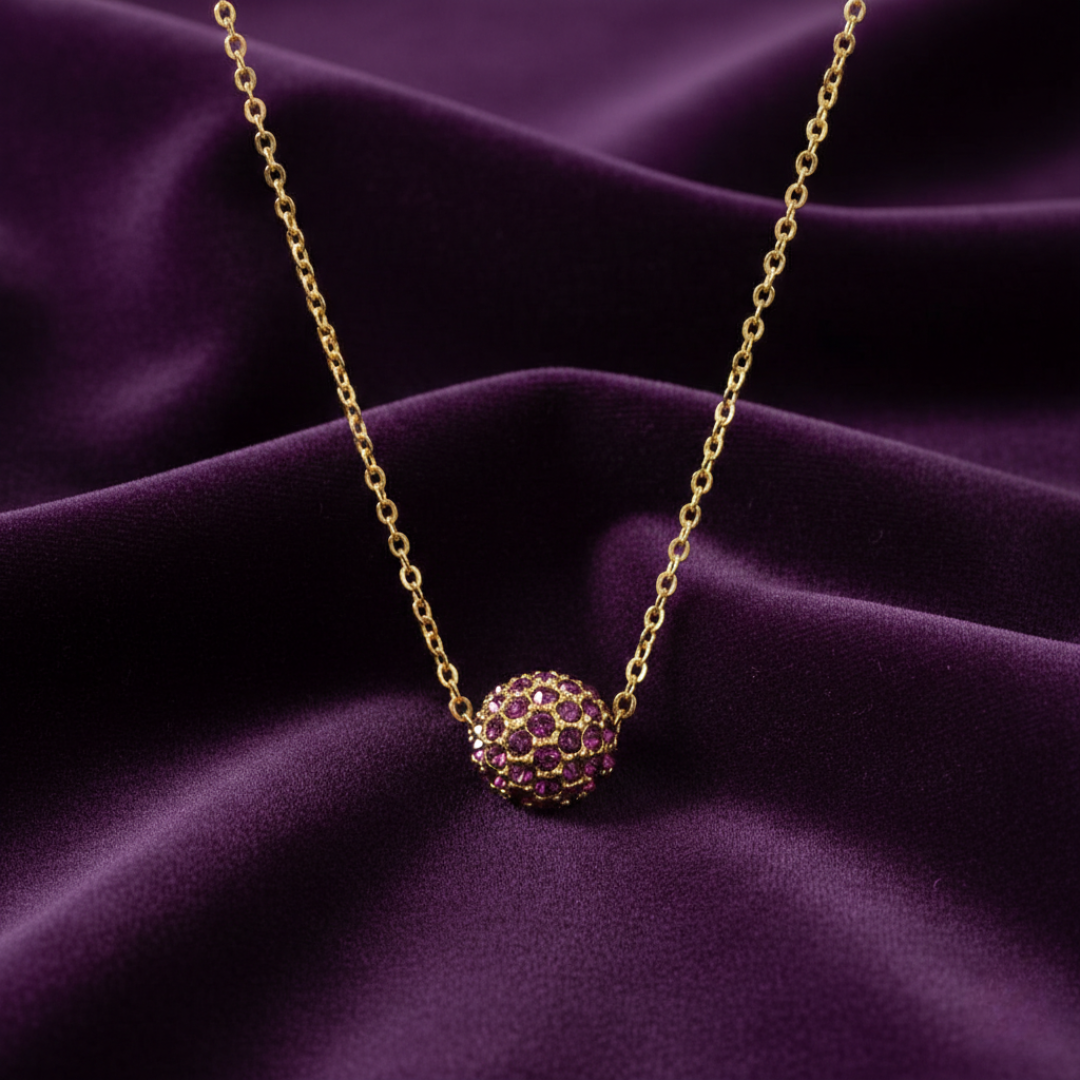 Gold necklace with a purple crystal pendant on a purple fabric background