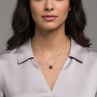 Woman wearing a gold necklace with a purple crystal pendant against a gray background