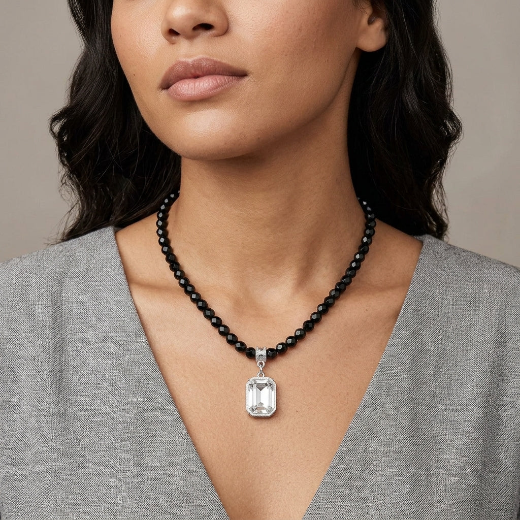 Woman wearing a black beaded necklace with a silver crystal octagon pendant against a neutral background
