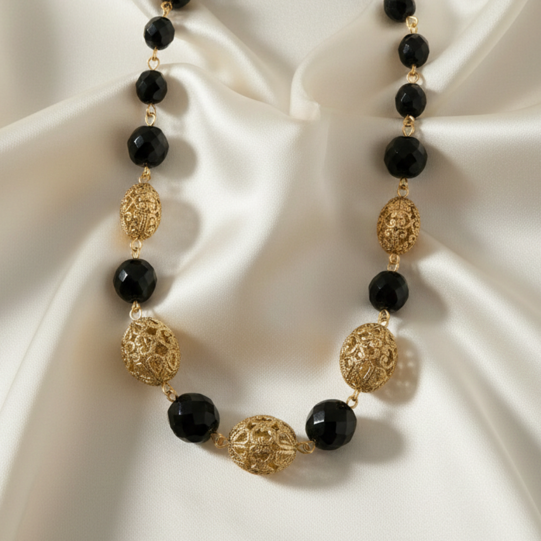 Necklace with black beads and gold filigree on a white fabric background