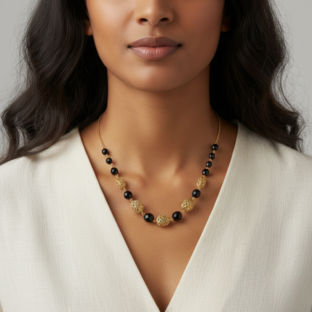 Woman wearing a gold and black beaded necklace against a neutral background