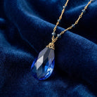 Faceted Sapphire Blue Glass Briolette Pendant & Beaded Necklace on a blue fabric background