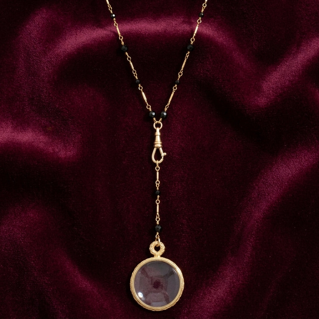 Black Bead Magnifying Glass Drop Necklace on dark maroon fabric