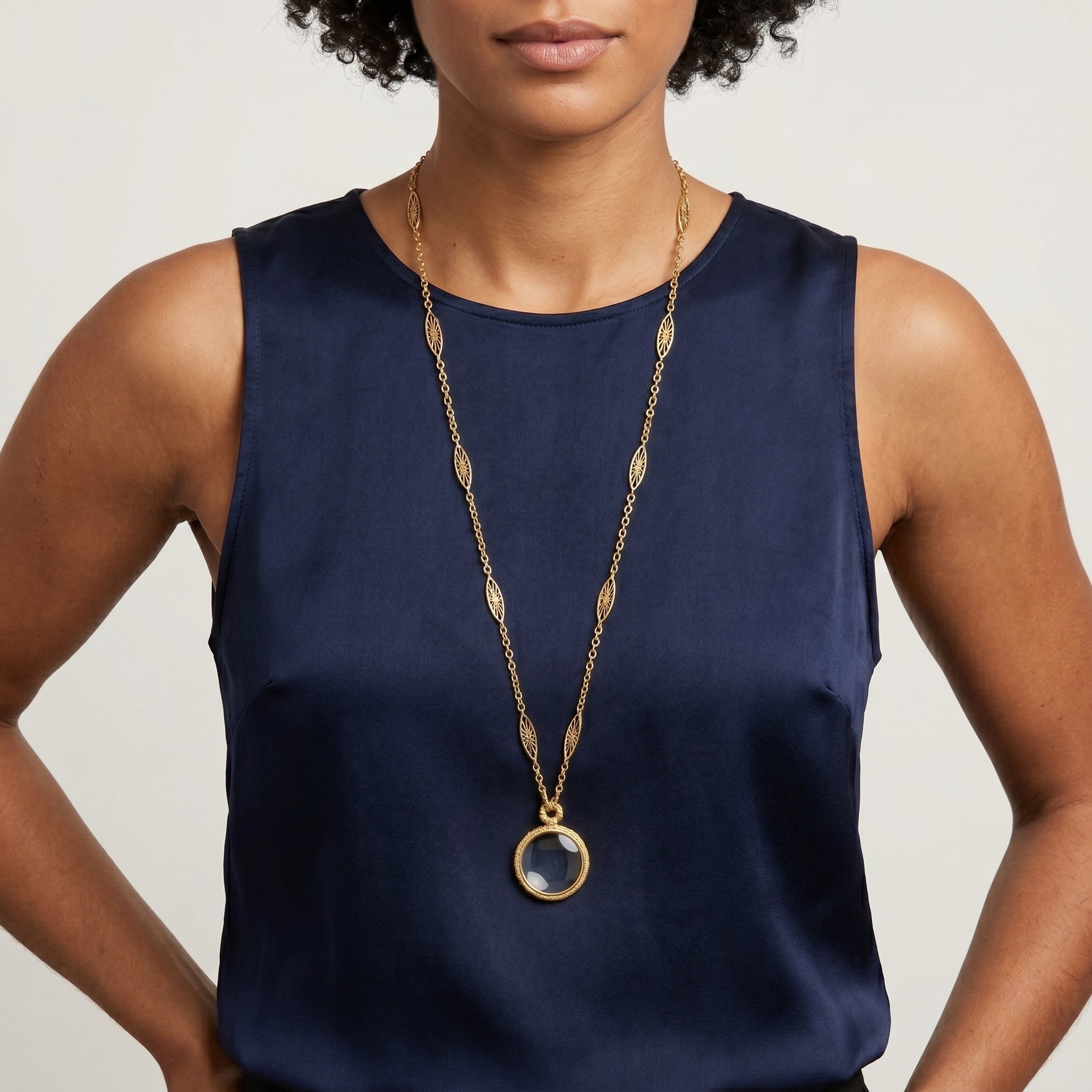 Filigree Chain Round Magnifying Glass Pendant Necklace worn by a woman in a sleeveless navy blue top