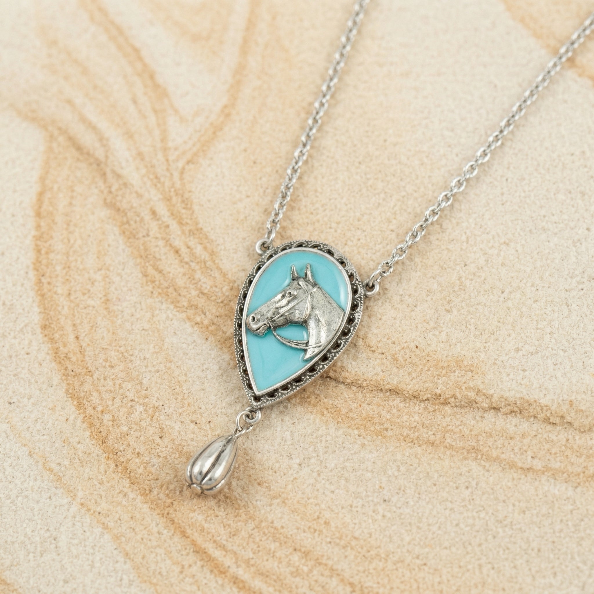 Southwest Turquoise Horse Head Pendant Teardrop Necklace resting on light sandstone 