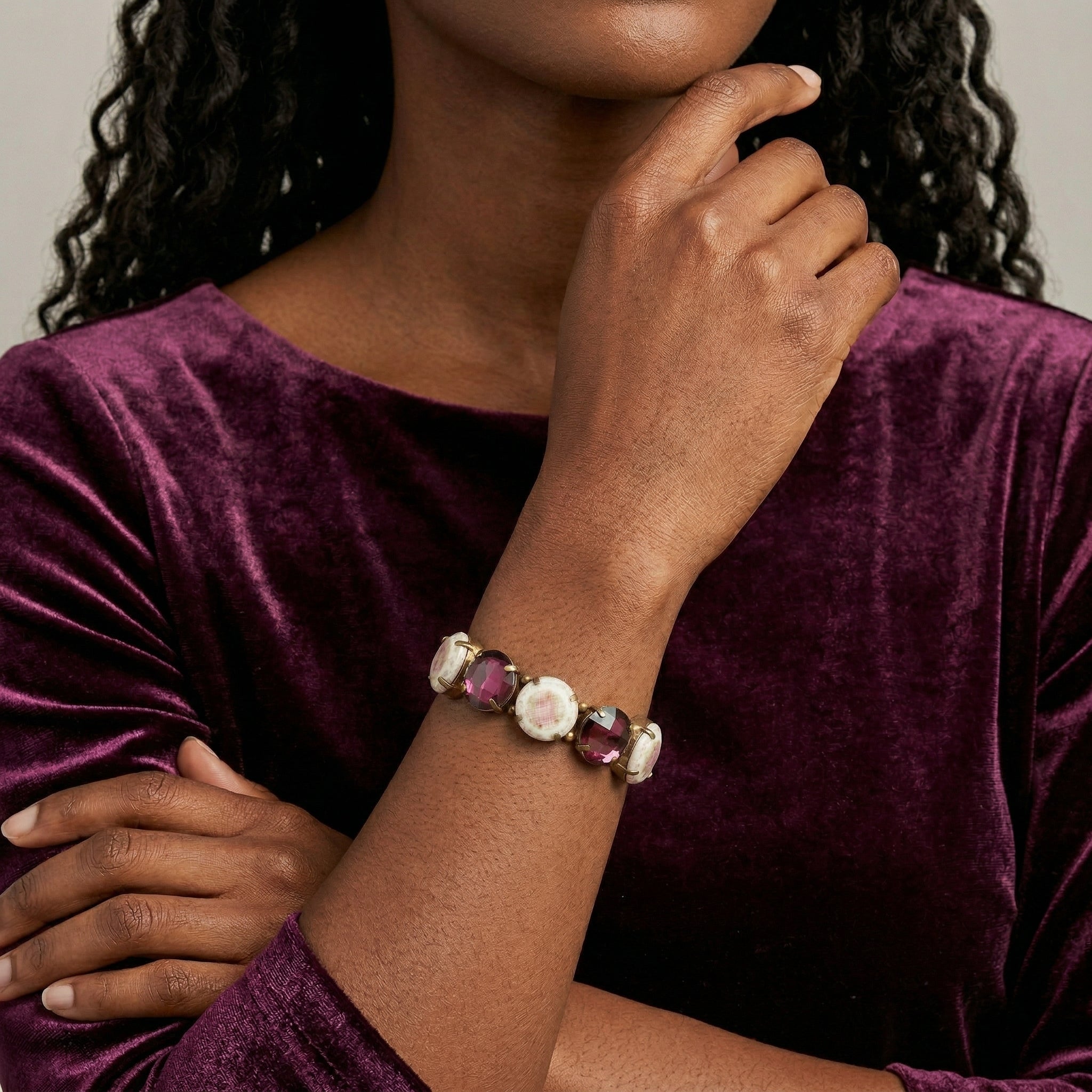 Woman wearing a bracelet with purple and white beads on a plain background