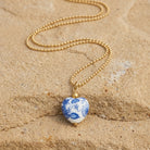 Necklace with a blue and white heart-shaped pendant on a sandy surface