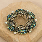 Peacock Plumage Blue Iridescent AB Glass Stone Wreath Brooch on a textured stone surface