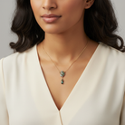 Woman wearing a gold necklace with a Peacock feather pendant against a neutral background.