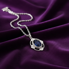 Silver necklace with a blue gemstone pendant on a purple fabric background