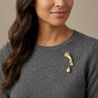 Woman wearing a gray sweater with a gold brooch featuring a pearl.