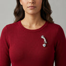 Woman wearing a red sweater with a Blue Willow style brooch on a gray background