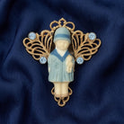 Blue crystal Winged Filigree Porcelain Child With Doll Pin on a dark blue fabric background