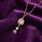 White Crystal Opal Stone 3 Sided Spinner Drop Necklace on a purple fabric background