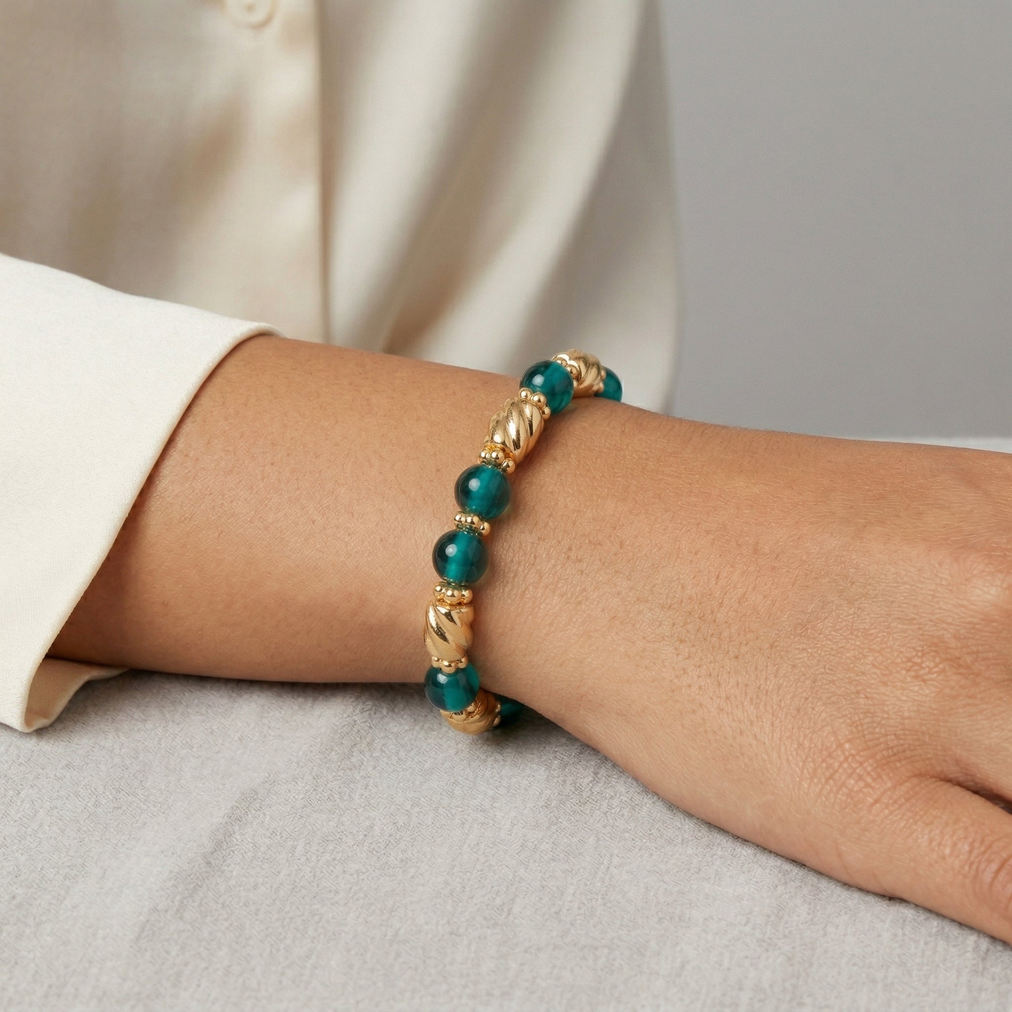 Teal Round Glass & Twisted Gold Tone Bead Bracelet on a wrist against a neutral background