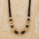 Black Fire Polished Strand Corrugated Bead Necklace on a beige stone surface