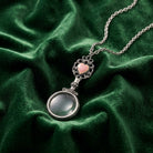 Pink Heart Magnifying Glass Necklace resting on dark green fabric