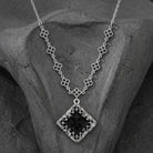 Belladonna Black Glass Stone Filigree Pendant Necklace resting on dark stone