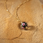 Necklace with a glass bead pendant that has a floral design on a sandy stone surface