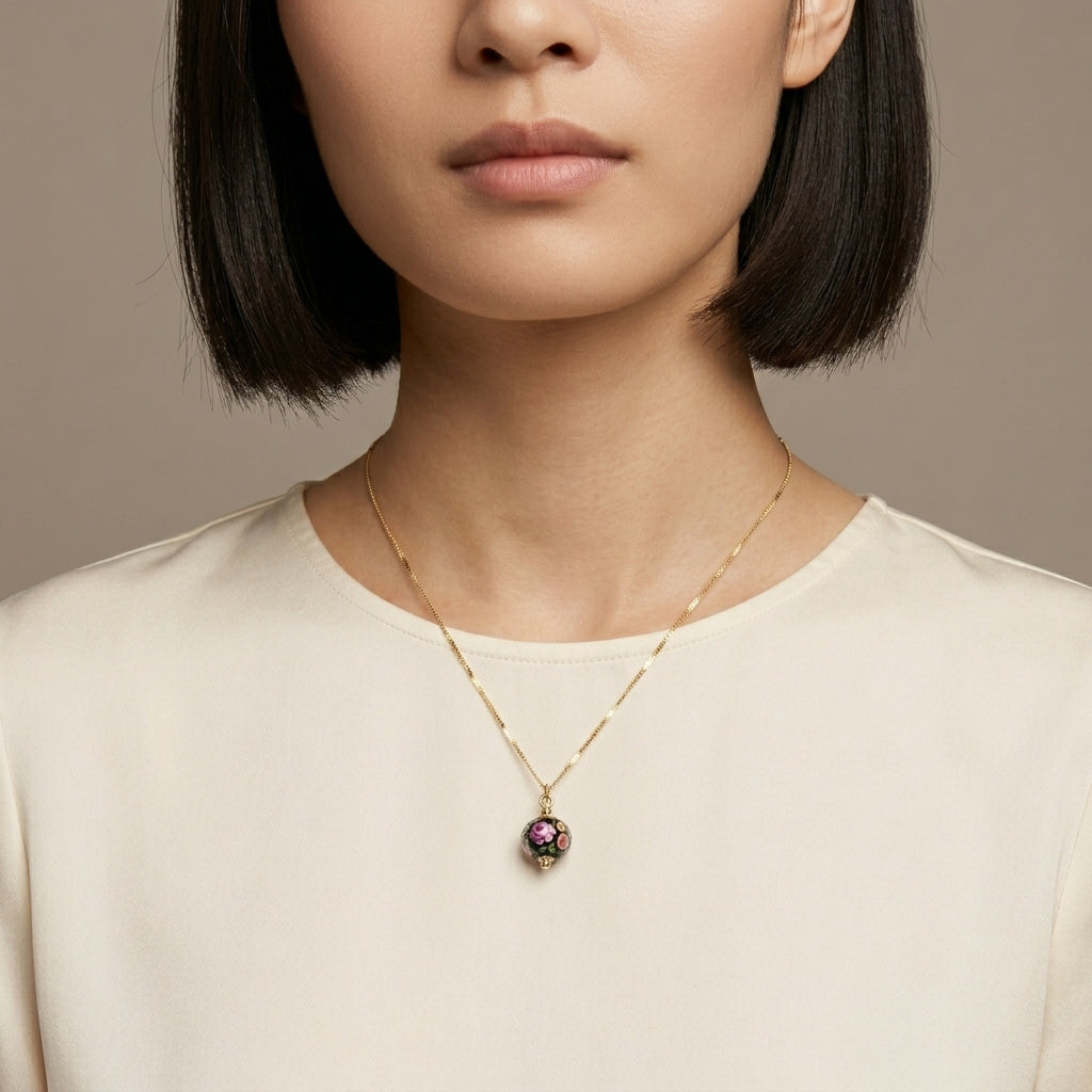 Woman wearing a gold tone necklace with a black glass bead pendant against a neutral background