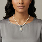 Woman wearing a pearl necklace with a gray top against a neutral background