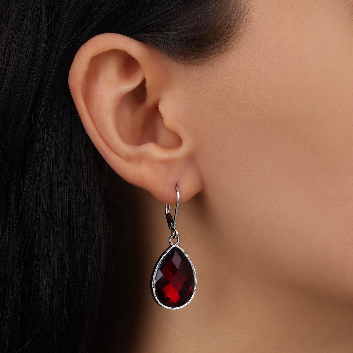 A close-up of a model's ear wearing a Silver Faceted Siam Red Stone Teardrop Earrings