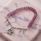 Pink beaded bracelet with paw charm and 'LOVE' letters on a marble surface