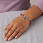 Hand wearing a bracelet with paw print charm and 'LOVE' letters on a gray surface.