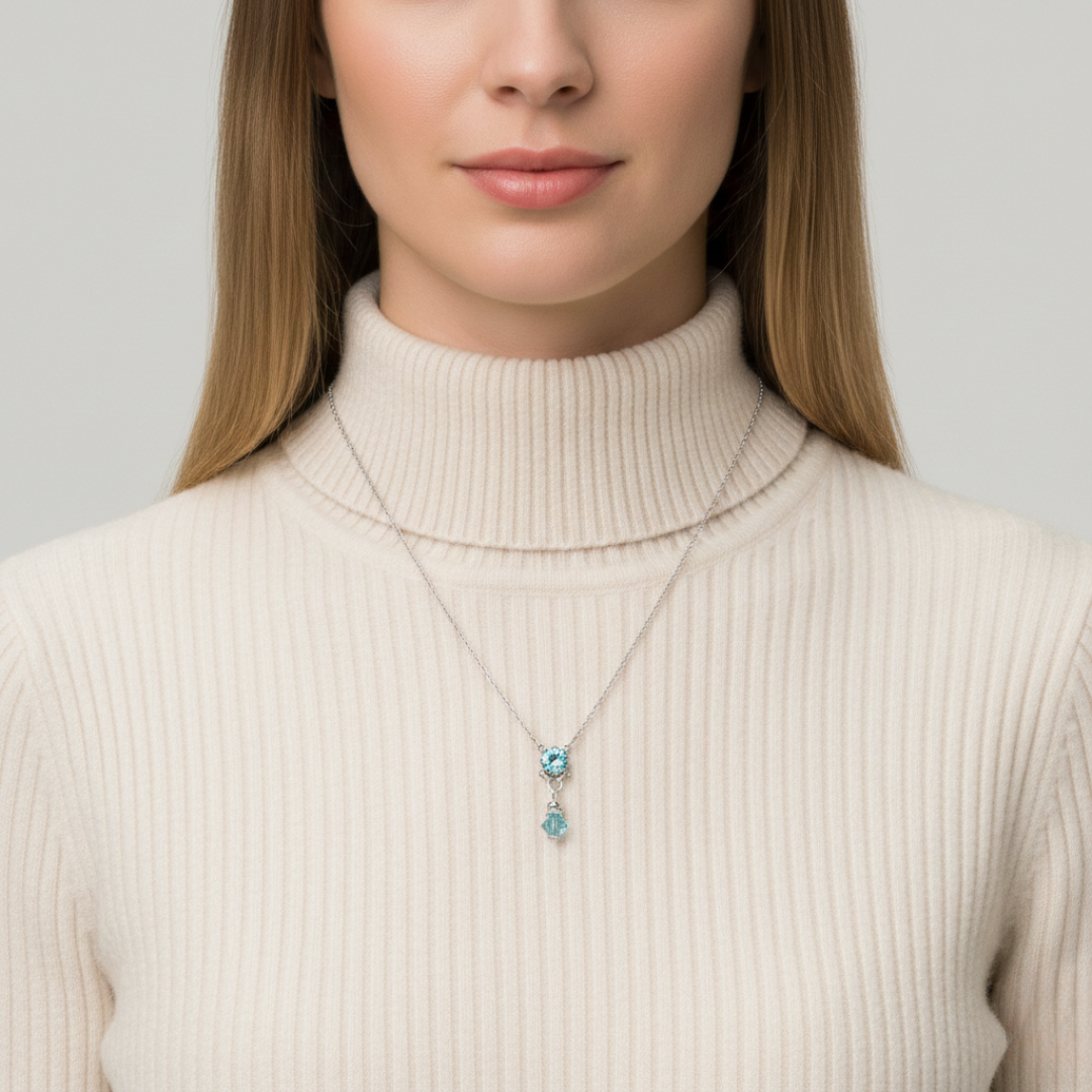Woman wearing a beige turtleneck sweater with a necklace featuring blue gemstones against a neutral background