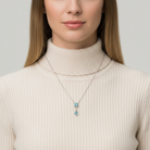 Woman wearing a beige turtleneck sweater with a necklace featuring blue gemstones against a neutral background