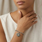 Woman wearing a bracelet with a heart-shaped horse head charm on a neutral background
