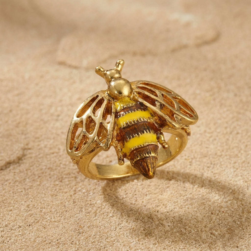 Gold tone bee-shaped ring on a beige sand background