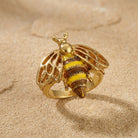 Gold tone bee-shaped ring on a beige sand background