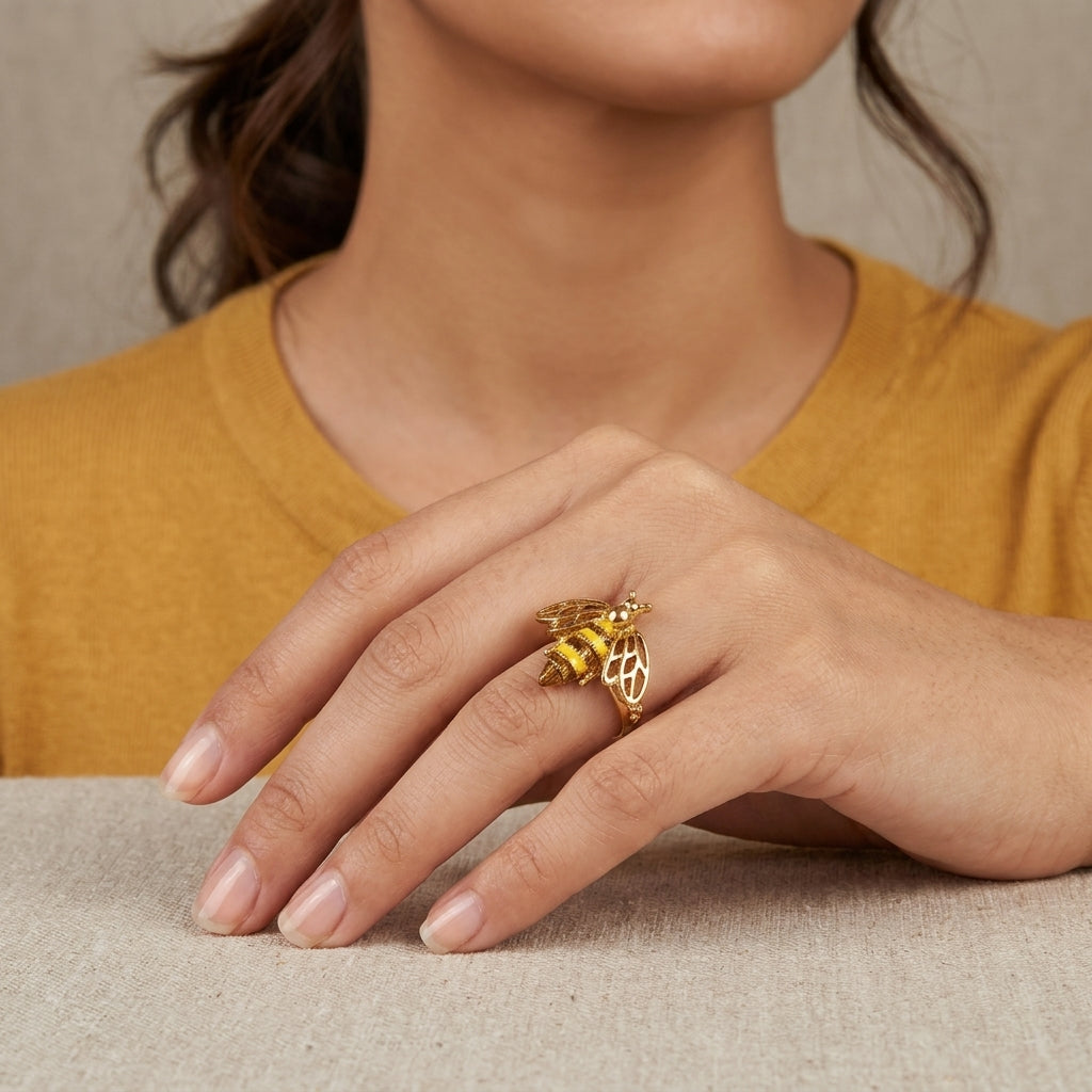 Close-up of a hand wearing a gold tone ring with a bee design, against a neutral background.
