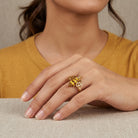 Close-up of a hand wearing a gold tone ring with a bee design, against a neutral background.