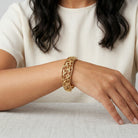 Woman in a white outfit showing a Gold Floral Hinge Bracelet on her wrist