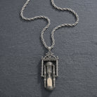 Pewter silver tone hourglass pendant with sand inside resting on a dark stone surface