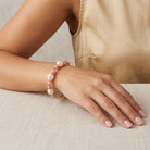 Hand wearing a pink pearl bracelet on a neutral background