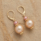 Raspberry and champagne colored bead earrings with gold tone accents resting on a sandstone surface