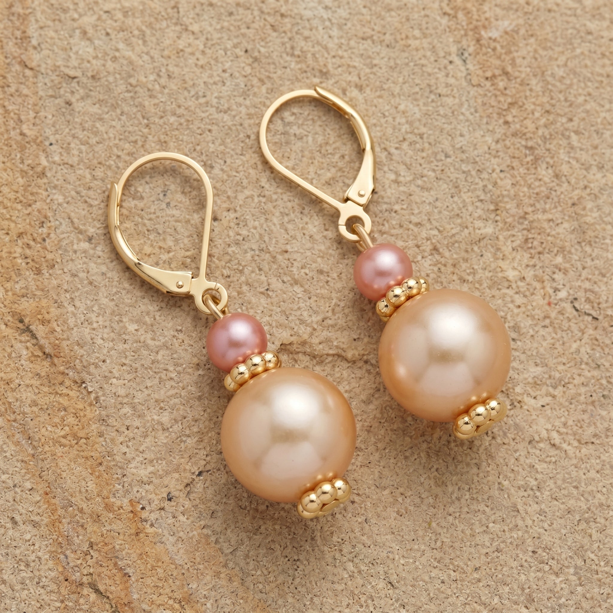 Raspberry and champagne colored bead earrings with gold tone accents resting on a sandstone surface