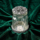 Decorative glass jar with a silver lid on a green fabric background