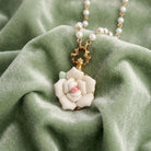 White Garden Porcelain Rose Faux Pearl Necklace resting on light green fabric