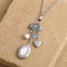 Aquamarine Crystal Mother Of Pearl Charms And Locket Necklace resting on sandstone surface