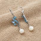 Aquamarine Crystal Mother Of Pearl Dangle Earrings displayed on a textured beige fabric background.