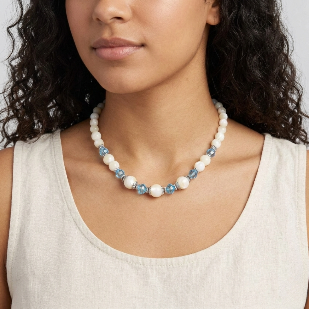 Woman wearing a necklace with white faux pearls and blue beads against a neutral background