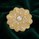 Gold tone iImperial Flower Crystal Brooch with clear crystals resting on dark green fabric