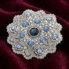 Imperial Silver Tone Flower Blue Crystal Brooch resting on dark red fabric