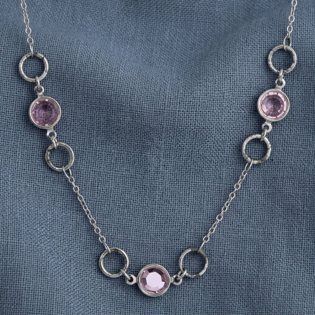Light Amethyst Channel Crystal & Ring Chain Necklace resting on a dark blue linen fabric