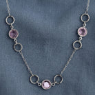 Light Amethyst Channel Crystal & Ring Chain Necklace resting on a dark blue linen fabric