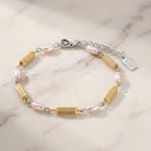 Faux Pearl Rice Bead & Cylindrical Gold Tone Bead Link Bracelet resting on white marble surface